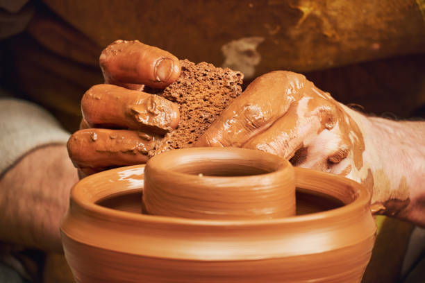 A man in old medieval Byzantine clothes sits behind a vintage potter's wheel and makes dishes out of clay. Pottery in nature in retro style.